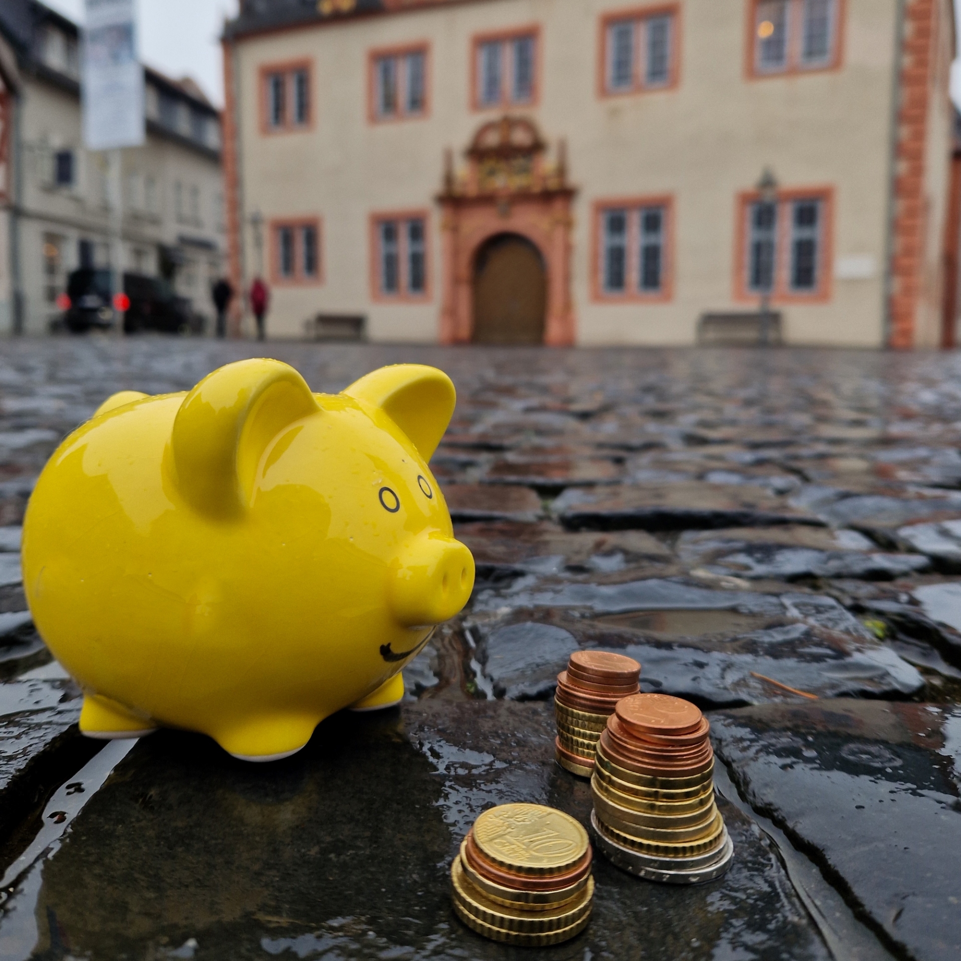 Foto: Gelbes Sparschwein mit Kleingeld vor Rathaus