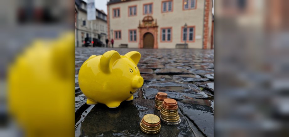 Foto: Gelbes Sparschwein mit Kleingeld vor Rathaus